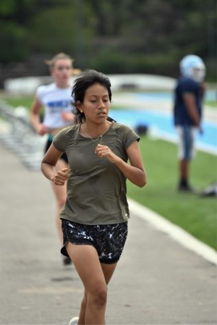 Sophomore Diana Zumba runs  around the track during practice on May 19 while the football team conducts spring practice on the turf field.  A track with no markings or rubber surface is one of several challenges faced by the track programs in 2021.